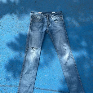 Replay ljusblå slitna jeans - Säljer ett par ljusblå jeans från Replay med slitningar och hål på ena benet. Klassisk femficksmodell med raka ben och snygg tvätt. Jeansen har detaljer som slitna partier och Replay-lapp bak i midjan. Perfekta för en avslappnad streetstil. Jag är 180 och dem passar 