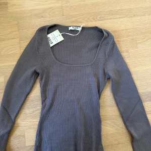 Ribbad grå långärmad tröja NA-KD - Supersnygg ribbad grå tröja från NA-KD med fyrkantig urringning och lång ärm. Tröjan har en tight passform och är tillverkad i mjuk, stretchig bomullsblandning. Perfekt att styla med jeans eller kjol för en clean look.