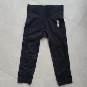 Svarta seamless gymtights från Gymshark - Svarta seamless tights från Gymshark med hög midja och snygga meshdetaljer längs benen. Modellen är trekvarts och har en tight passform som sitter skönt vid träning. Gymshark-logga på höften och bak på linningen.