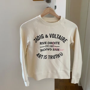 Vit tjocktröja från Zadig & Voltaire - Säljer min vita sweatshirt från Zadig & Voltaire med svart tryck framtill. Tröjan har rund hals, långa ärmar och en klassisk, relaxed passform. Materialet är mjuk bomull som känns skönt mot huden. Perfekt för dig som gillar stilrena och coola statement-plagg. Den är i storlek 12 år och passar någon med storleken 152-158 ca❤️ Nästan helt oanvänd (använt ca 2 gånger) dvs den är i topp skick!