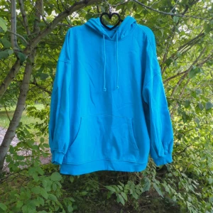 Blå hoodie från H&M Divided - Chill blå hoodie från Divided H&M i storlek S, oversized modell. Tröjan har huva med snörning, stor magficka och långa ärmar med muddar. Materialet är 60% bomull och 40% polyester, vilket gör den både mjuk och skön. Perfekt för dig som gillar enkel och stilren streetwear.  Den är varm och gosig inuti så passar även utmärkt till kallare vinterdagar och sent en sommarkväll. ☀️🥶  Katter finns i hemmet. 