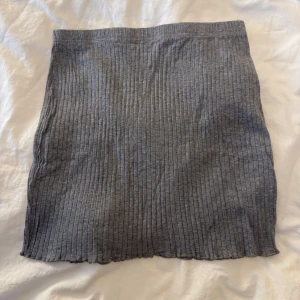 Grå ribbad kortkjol - En enkel och stilren grå ribbad kortkjol i mjukt material. Kjolen har en rak passform och är perfekt att matcha med en oversized hoodie eller en tight topp. Snygg till sneakers eller boots för en chill look.