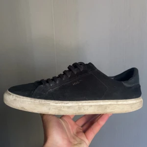 Svarta sneakers från Axel Arigato - Säljer ett par svarta sneakers från Axel Arigato med stilren design och låg profil. Skorna har ovandel i mocka, platt vit sula och klassisk snörning. Perfekt för dig som gillar minimalistisk stil och vill ha ett par schyssta sneakers med diskret branding på sidan. (Jag möts upp i Stockholm och tar endast swish)