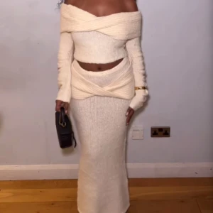 Vit stickat offshoulder set - Trendig vit stickad klänning med offshoulder-design och lång ärm. Klänningen har en unik omlott-detalj vid midjan och är croppad för en modern look. Materialet är strechigt. Helt oanvänt med etiketter kvar.