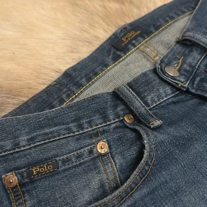 Blå jeans från Polo Ralph Lauren - Snygga blå jeans från Polo Ralph Lauren med klassisk femficksdesign och knappgylf. Perfekta för en avslappnad stil med fantastiskt fin passform . Märkeslogga på bakfickan storlek 30x34. Nästintill nya används 1 gång och tvättade 1 gång anledningen till varför jag säljer är att de är lite små i midjan för mig. Nypris på dessa ligger på 1900 kr men mitt pris är endast 399kr passa på medan de finns kvar! 