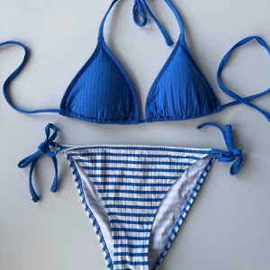 Blå randig bikini med knytband - Oanvänd! Snygg blå bikini med randigt mönster och knytband. Överdelen har en ribbad struktur och trekantsform, medan underdelen har knytband i sidorna för justerbar passform. Perfekt för sommarens stranddagar! Nypris 449:- 