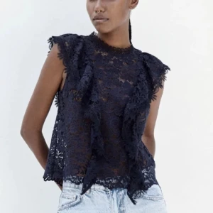 Mörkblå spetsblus - Elegant mörkblå spetsblus med volangdetaljer. Blusen är ärmlös och har en vacker, genombruten spetsdesign som ger en romantisk känsla. Perfekt för att lyfta vilken outfit som helst.