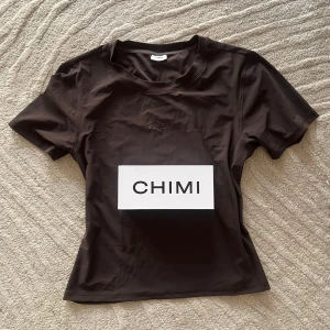 CHIMI | Body T-shirt i träningsmaterial - Snygg mörkbrun t-shirt från CHIMI med korta ärmar och rund hals. Perfekt för en stilren look. Logotypen är diskret placerad på bröstet. Endast testad, aldrig använd! Material: 74% Polyamide (recycled) / 26% Elastane. Köptes för 800kr!