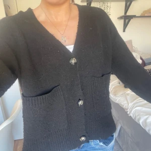 Svart kofta med knappar - Mysig svart kofta med stora knappar och två framfickor. Perfekt för kyliga dagar och enkel att matcha med jeans eller kjol.