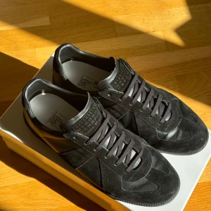 Svarta sneakers från Maison Margiela - Snygga svarta sneakers från Maison Margiela i en kombination av mocka och skinn. Skorna har en rund tå och klassisk snörning. Perfekta för en stilren look. Använda 2-3 gånger, box & 2 dustbags medföljer. 