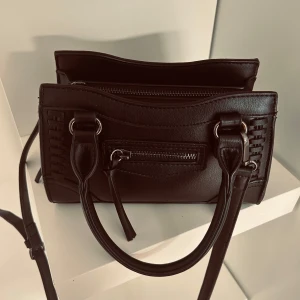 Svart axelväska med dragkedja - Snygg svart axelväska i skinn med praktisk dragkedja och stilrena handtag. Perfekt för att bära dina nödvändigheter med stil. Enkel och elegant design som passar till många tillfällen.