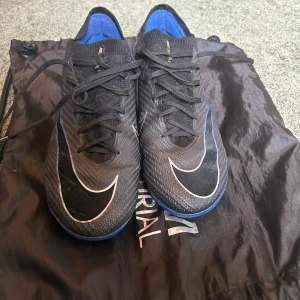 Nike Mercurial fotbollsskor - Nike Mercurial konstgräs fotbollsskor i svart och blått. Skorna har täcken på användning men ingen större skada. Gympapåsen följer med! Ny pris 3149kr, kvitto finns!