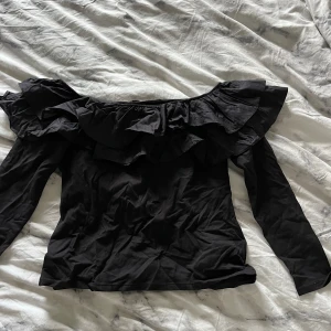 Svart offshoulder topp med volang - Säljer en snygg svart topp från H&M med volangdetaljer runt halsen.  Lägg gärna prisförslag! Storlek L men är som S-M