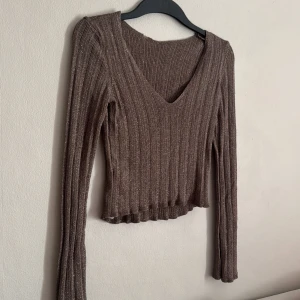 Brun ribbad tröja - Säljer en brun ribbad tröja med v-ringning och långa ärmar. Tröjan är croppad och har en glittrig finish som ger den en extra touch. Perfekt för att lägga till lite stil i din garderob.