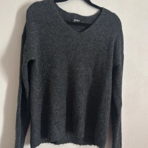 Grå stickad tröja från ONLY - Säljer en mysig grå stickad tröja från ONLY med v-ringning. Perfekt för kyliga dagar och enkel att matcha med olika outfits. Tröjan har långa ärmar och en avslappnad passform.