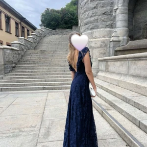 Marinblå spetsklänning - Elegant marinblå långklänning i spets med volangdetaljer. Perfekt för formella tillfällen. Klänningen har en v-ringad design och är ärmlös, använd 1 gång.