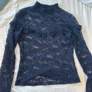 Mörkblå volang och spetsblus, Spetstopp - Elegant mörkblå spetsblus med volangdetaljer och lite krage. Blusen har långa ärmar och ett vackert blommönster i spetsen. Köpt på Plick men aldrig använt💞💞