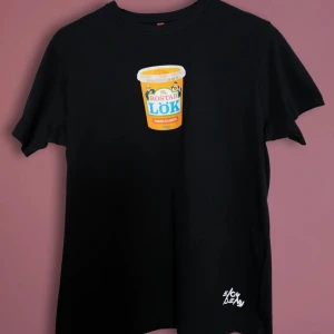 Elov & Beny Raggen går T-Shirt Storlek XS - Snygg svart t-shirt med ett humoristiskt tryck av en burk rostad lök på framsidan och texten 'Raggen Går' på baksidan. Perfekt för dig som gillar att sticka ut med en rolig stil. Tillverkad av mjukt material för en bekväm passform. Storlek XS