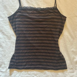 Svart och brun randig linnetopp - Säljer detta brun- och svartrandiga linne då det tyvärr inte är min stil längre. Sitter figurnära på mig som brukar ha m/s fina spetsdetaljer längst upp och i bra skick