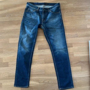 Blå jeans från Tiger of Sweden - Säljer ett par snygga blå jeans från Tiger of Seden. De har en klassisk femficksdesign och en läderpatch med logotyp baktill. Jeansen har en normal passform och är tillverkade i denim med en lätt tvättad look.