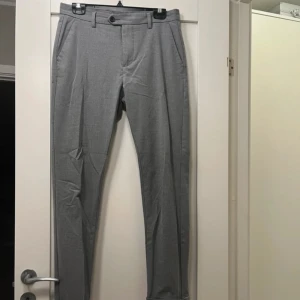 Grå kostymbyxor från Jack & Jones - Snygga grå kostymbyxor från Jack & Jones i modellen Slim Marco. Byxorna har en slim passform. Har två små fläckar som syns på bilderna. 