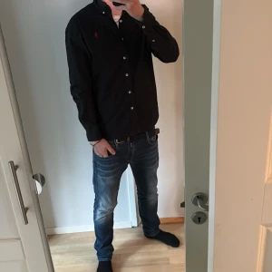 Svart skjorta från Polo Ralph Lauren - Säljer en stilren svart skjorta från Polo Ralph Lauren i slim fit. Skjortan har långa ärmar och knappar framtill. Perfekt för en elegant look.