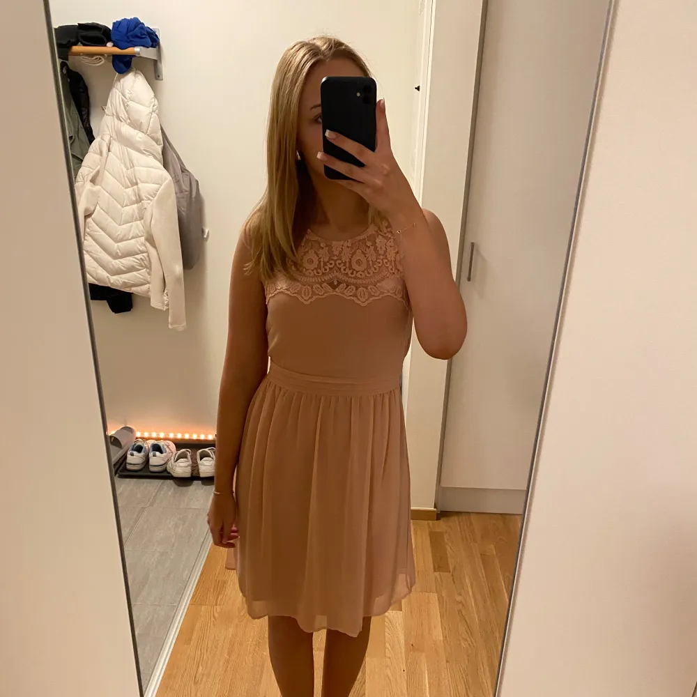 Säljer en söt beige klänning med vacker spets upptill. Klänningen är ärmlös och har en kort längd som passar perfekt för sommarens festligheter. Den har en rund halsringning och ett lätt och luftigt material.. Mekot.