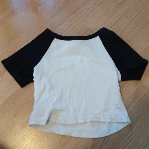 Svart och vit kortärmad topp - Säljer en svart och vit kortärmad topp. Toppen har en klassisk raglanstil med svarta ärmar och vit kropp. Perfekt för en avslappnad stil. Storlek xs