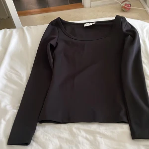 Svart långärmad topp från VILA - Säljer en stilren svart långärmad topp från VILA. Toppen har en rund halsringning och är perfekt för både vardag och fest. Tillverkad i ett mjukt och bekvämt material.