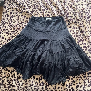 Svart volangkjol - Säljer en svart kjol med flera lager av volanger. Kjolen har en luftig och fladdrig design som ger en bohemisk känsla. Perfekt för att skapa en avslappnad och stilfull look.