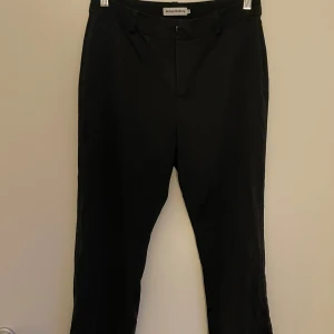 Svarta kostymbyxor i silke från Ahlvar Gallery - Croppade svarta kostymbyxor i strl S. De har en klassisk design med dragkedja och hällor för bälte. 90% silke 10 % spandex. Inköpta för ca 2000:-