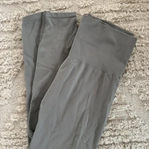 Grå/khaki leggings/träningstights - Snygga grå/khaki leggings/träningstights med hög midja och ribbad detalj. Perfekta för en bekväm och stilren look. Passar utmärkt till både träning och vardagsbruk.