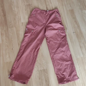 Rosa cargopants - Snygga rosa cargopants med flera fickor och knappdetaljer. Byxorna har en loose passform och justerbar midja med snörning. Perfekta för en avslappnad stil.