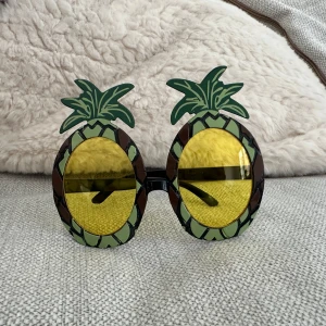 Ananasformade solglasögon - Roliga solglasögon i form av ananaser med gula linser och gröna detaljer. Perfekta för en somrig look eller temafest. Glasögonen har en unik design som garanterat drar blickarna till sig.