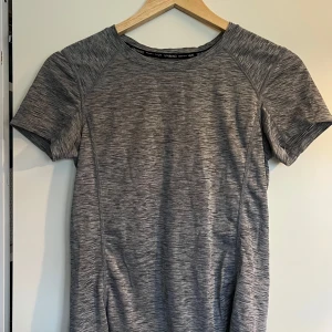grå träningströja - tränings t-shirt som är väl använd men i fint skick och självklart tvättad. lite längre modell. längd från axeln - 57 cm fram, 65 bak. bredd - 36 cm
