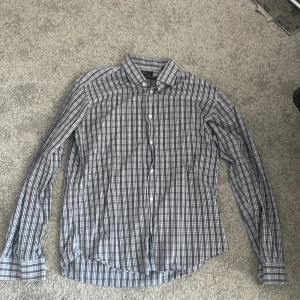 Rutig skjorta från Ben Sherman - Säljer en stilren rutig skjorta från Ben Sherman i blått och vitt. Skjortan har långa ärmar och knappar framtill. Perfekt för en klassisk look.