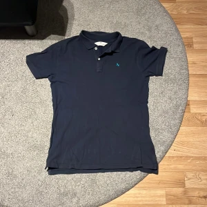 Mörkblå pikétröja från H&M - Säljer en stilren mörkblå pikétröja från H&M. Tröjan har korta ärmar och en klassisk krage med knappar. Perfekt för en avslappnad men ändå snygg look. 💙