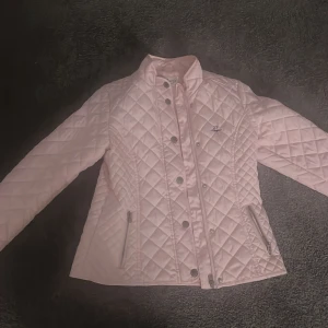 Rosa quiltad jacka från Hampton Republic - Säljer en snygg rosa quiltad jacka från Hampton Republic. Jackan har långa ärmar och stängs med knappar framtill. Två praktiska fickor med dragkedja på sidorna. Perfekt för en stilren look!