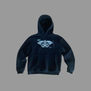 Svart hoodie med fjärilstryck - Snygg svart hoodie med ett unikt fjärilstryck på framsidan och text på baksidan. Perfekt för en avslappnad stil. Hoodien har en klassisk passform med långa ärmar och en praktisk magficka.