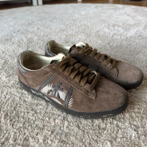 Bruna premiata skor - Säljer ett par bruna sneakers från premiata i mjuk mocka med svart sula och broderad detalj på sidan. Skorna har snörning och en unik design med kontrasterande insida i ljust skinn. Perfekta för dig som gillar stilrena men ändå unika skor.