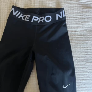 Svarta Nike Pro tights - Säljer ett par svarta Nike Pro tights med bred resår i midjan. Tightsen har en tight passform och är perfekta för träning. Klassisk Nike-logga på benet.