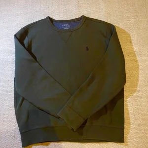 Ralph Lauren tröja - Säljer en fin mörkgrön sweatshirt från Polo Ralph Lauren med broderad logga på bröstet. Tröjan har långa ärmar och klassisk passform, perfekt för en stilren och avslappnad look.