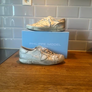 Vita sneakers från Philippe Model - Säljer ett par moderna Philippe Model sneakers med klassisk design och diskreta detaljer. Skorna har snörning, rund tå och platt sula. Tillverkade i skinn och levereras med originalkartong och dustbag. Skorna är väldigt slitna men designer är så från början. Men sedan har det självklart tillkommit slitningar när jag själv har använt dem. Därför det låga priset.