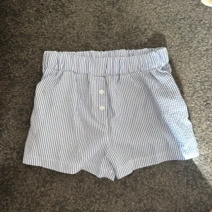 Blåvitrandiga shorts med knappar - Snygga blåvitrandiga shorts med resår i midjan och två vita knappar framtill. Tillverkade i ett lätt och luftigt bomullstyg, perfekta för varma dagar. Perfekt för stranden och soliga dagar! Aldrig använda 