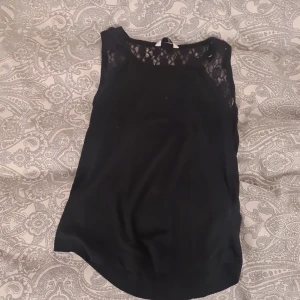 Svart ärmlös topp med spetsdetaljer - Säljer en svart ärmlös topp med fina spetsdetaljer upptill och på axlarna. Toppen har rund halsringning och är perfekt för dig som gillar en stilren look med lite extra detalj. Passar dig som är 13-14 år.🎀