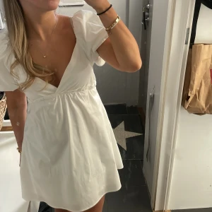 Studentklänning från Nelly - Superfin vit klänning med puffiga kortärmar och djup v-ringning. Klänningen har en lätt utställd kjol och markerad midja, vilket ger en feminin siluett. Perfekt för sommarens alla tillfällen och enkel att styla med smycken. Inga defekter! Köpte här på plick.