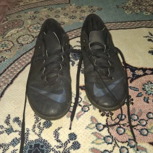 Svarta Nike Mercurial fotbollsskor - Säljer ett par svarta Nike Mercurial fotbollsskor med snörning och diskret Nike-logga på sidan. Skorna har en låg profil och är tillverkade i syntetmaterial för bra grepp och känsla på planen.