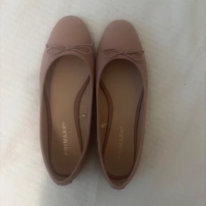 Beiga ballerinaskor med rosett från Primark - Säljer ett par klassiska beiga ballerinaskor från Primark. Skorna har en söt liten rosett framtill och rund tå. Perfekta för dig som gillar en enkel och stilren look.