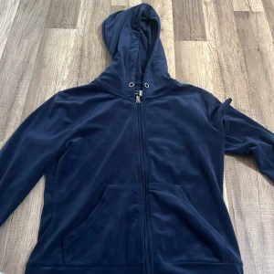 Mörkblå hoodie från Gina Tricot - Säljer en mörkblå hoodie från Gina Tricot i mjukt material. Tröjan har dragkedja framtill, huva med snörhål och två stora fickor. Perfekt för en avslappnad stil och enkel att matcha med jeans eller leggings.