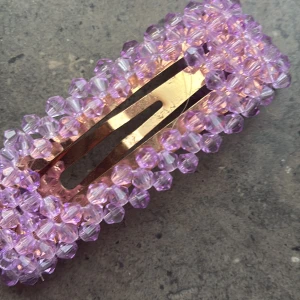 Lila pärlklämma - Säljer en snygg hårklämma dekorerad med lila pärlor. Klämman har en rektangulär form och en metallisk bas i guldton. Perfekt accessoar för att piffa upp frisyren.